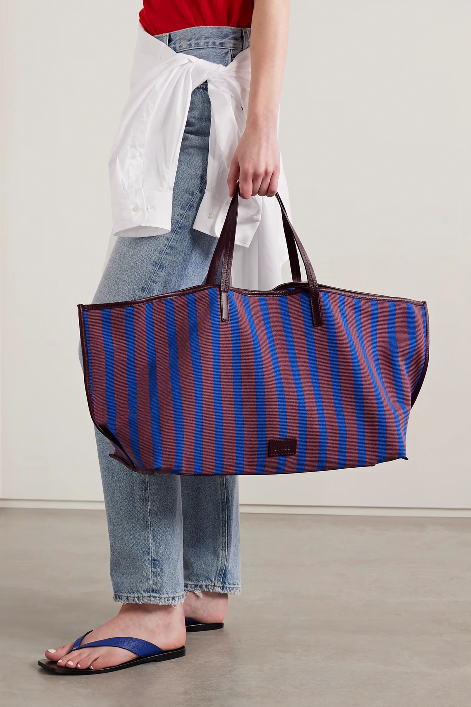 Person holding a large striped tote bag with a plain background