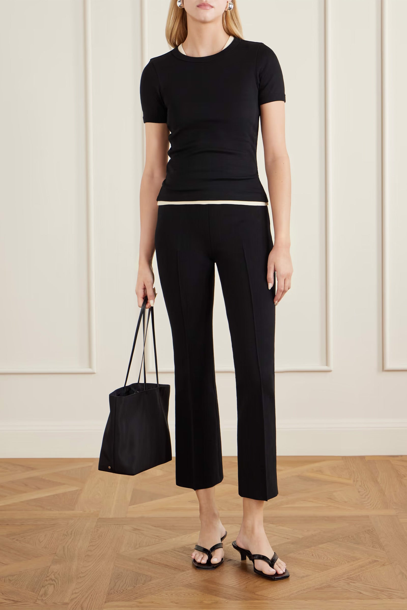 Woman wearing a black outfit holding a black handbag against a neutral background
