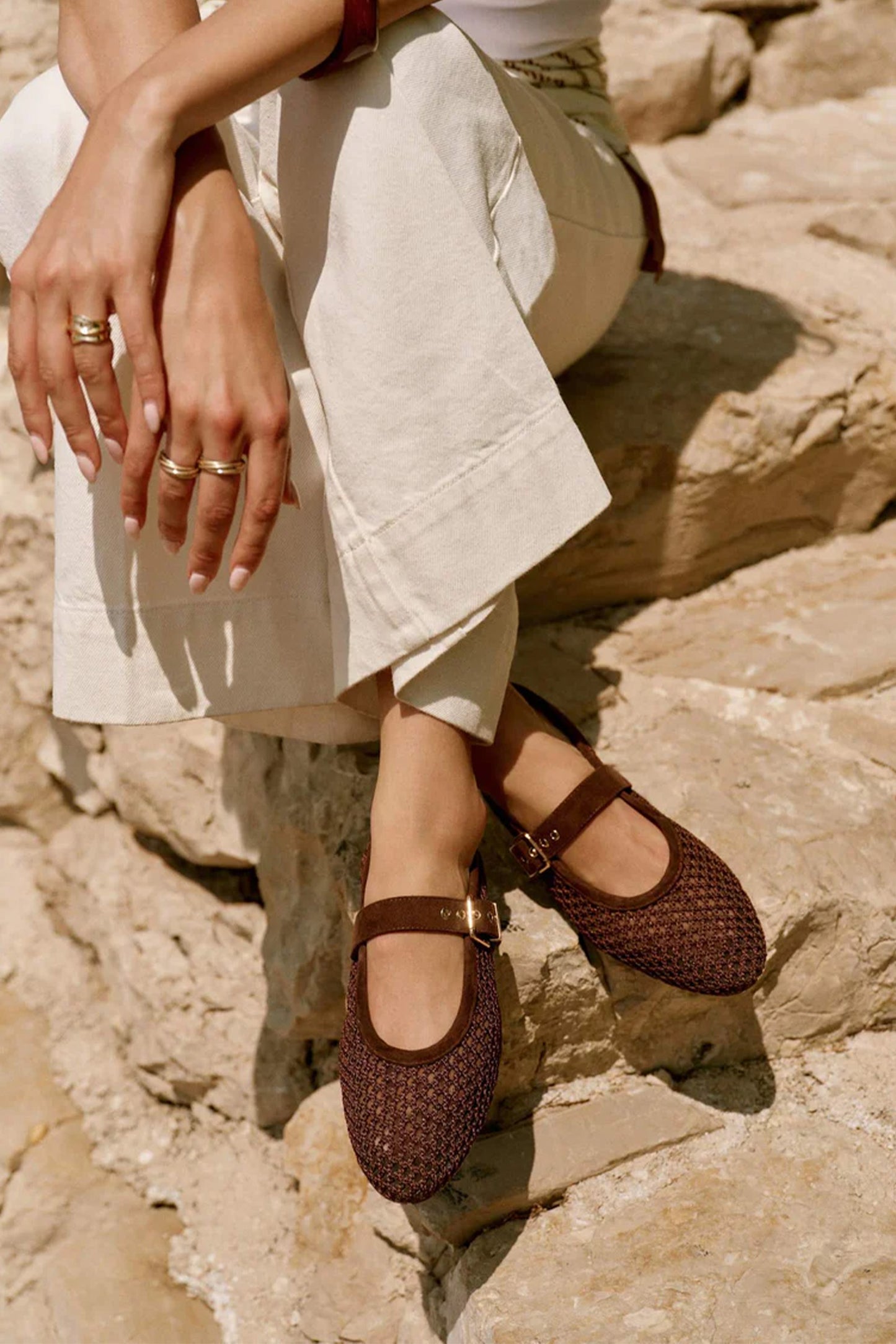 Person wearing brown woven shoes sitting on a rocky surface