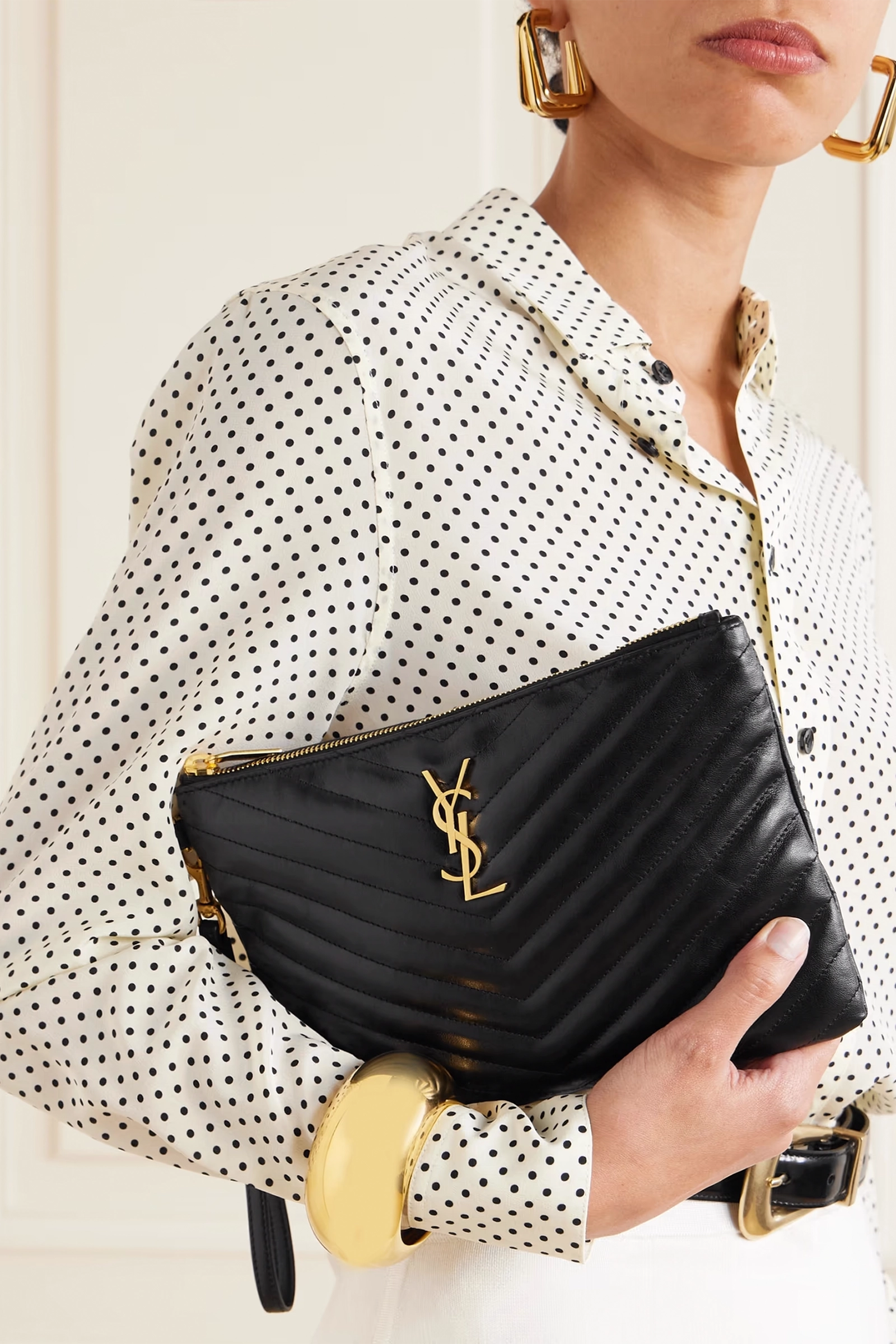 Person holding a black YSL clutch with gold accents against a neutral background